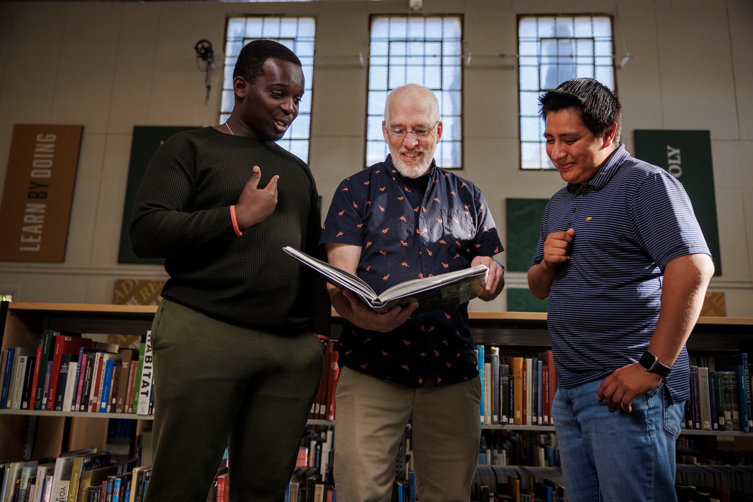 Students Einstein Mwase (left) and Luis Guzman (right) work with librarian Brett Bodemer in Crandall Gym, where the Kennedy Library is currently providing service to students during a renovation.
