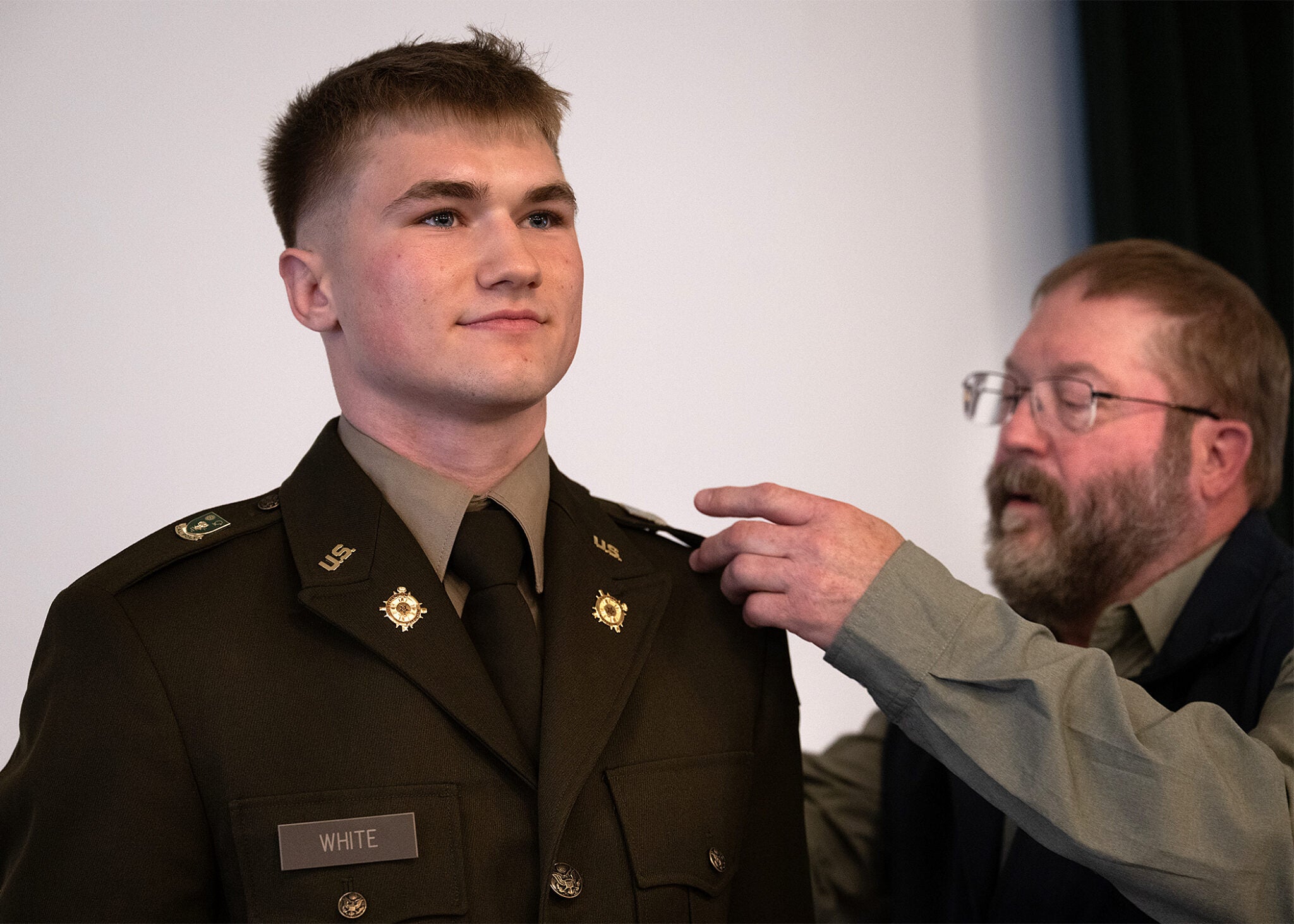 A proud family member pins an officer's insignia onto the shoulder of a newly commissioned Second Lieutenant named White in Army dress uniform during a Cal Poly ROTC commissioning ceremony.