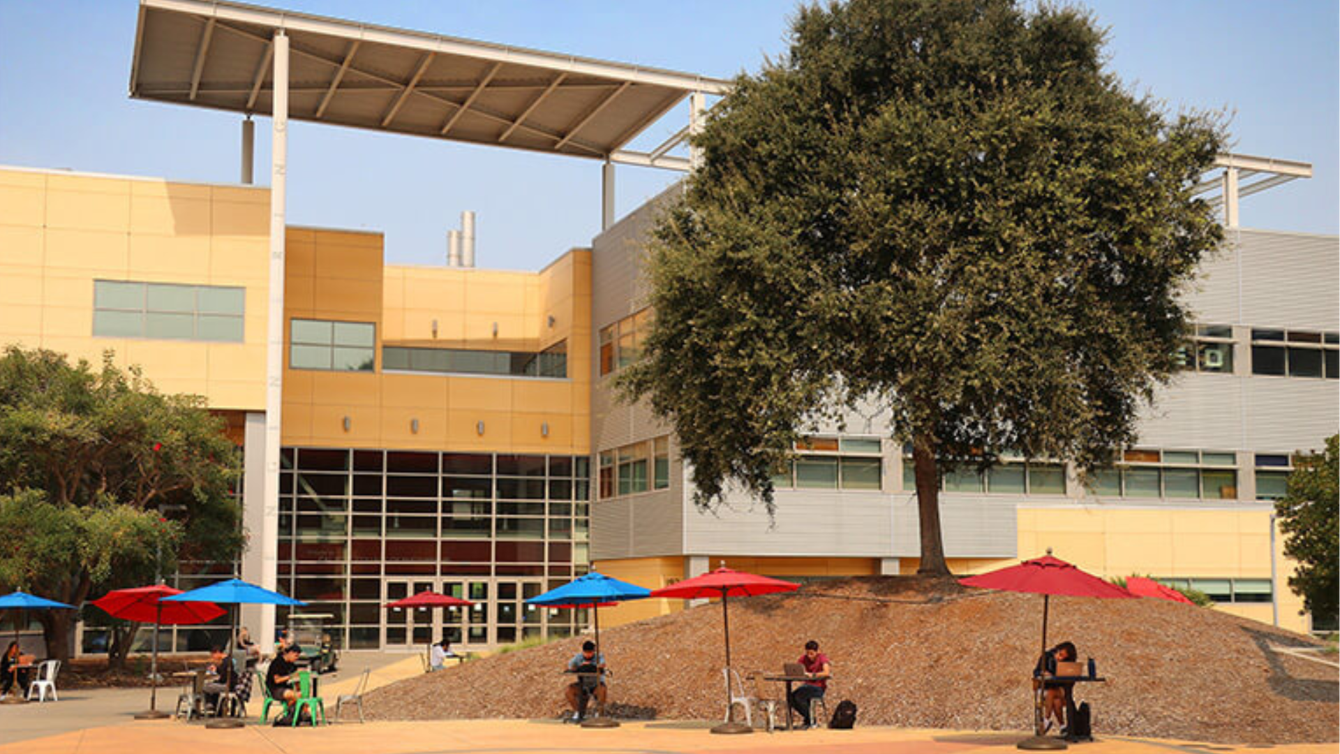 Students working at tables in the distance with the engineering 192 building in the background
