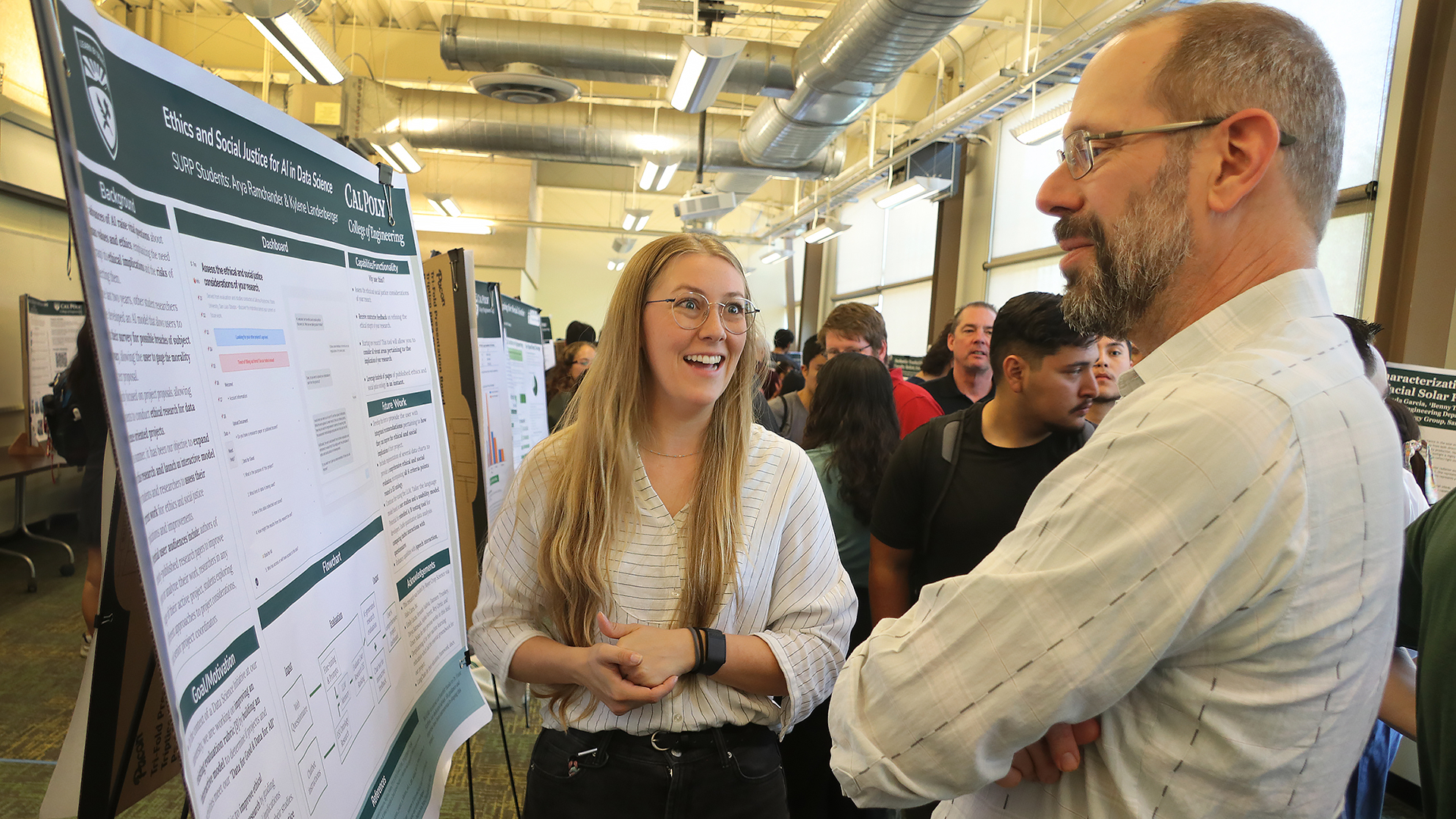 Professor talks to student about project poster during symposium