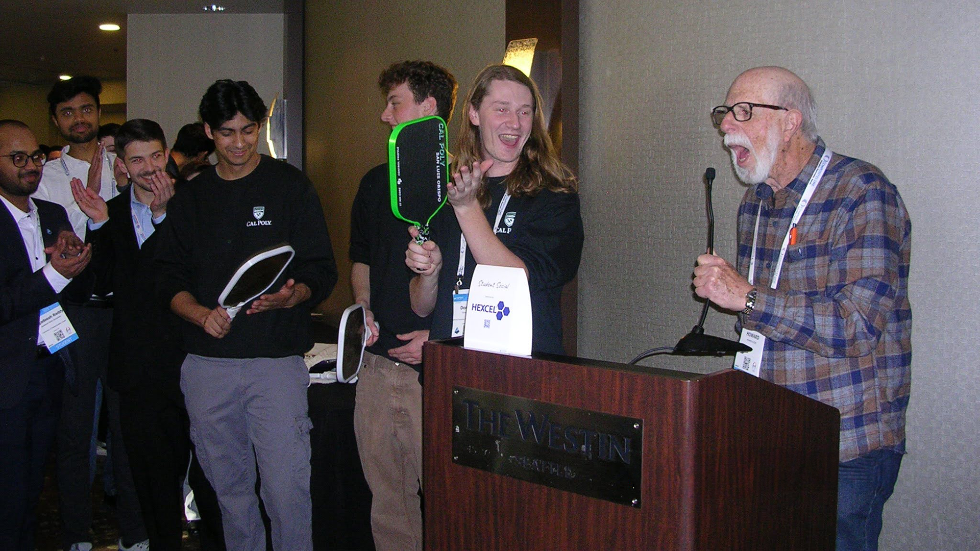 Donovan Furtado reacts as competition organizer Howard Kliger announces his first-place finish in SAMPE’s inaugural Student Pickleball Paddle Design Competition. Furtado holds his winning carbon fiber paddle during the awards ceremony. 