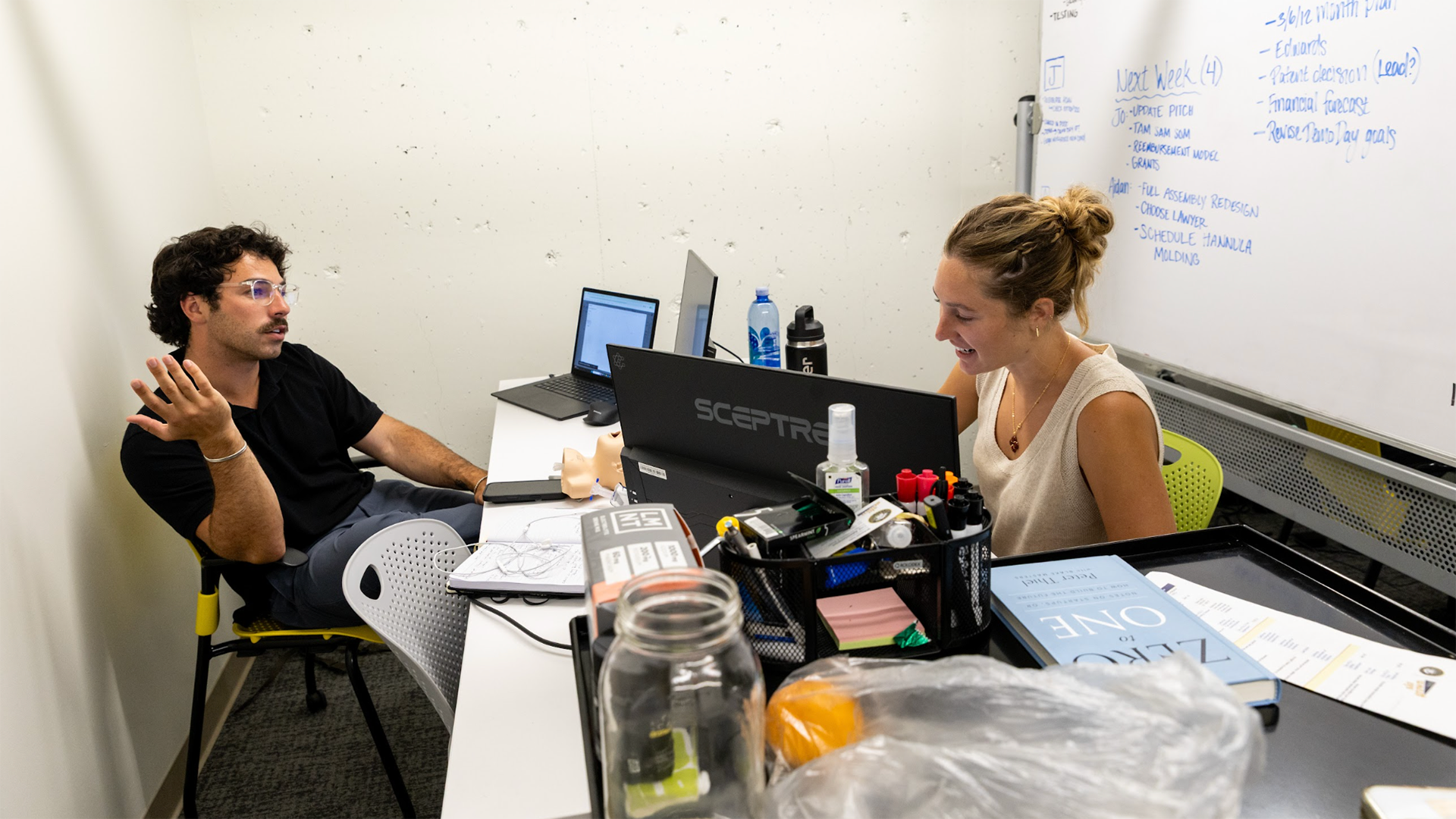 2 students work on laptops as they discuss progress