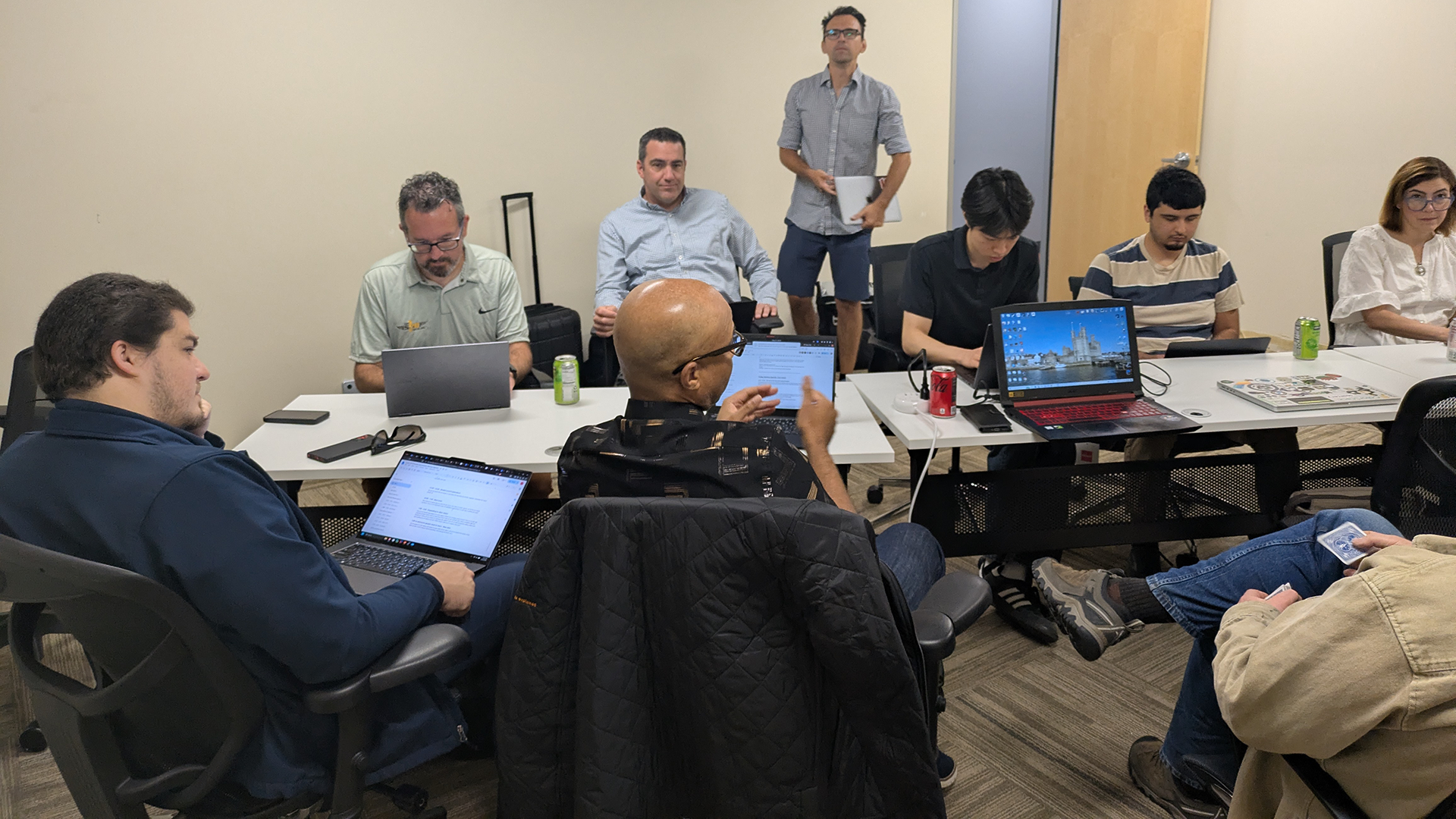 Team gathers around a worktable with laptops during a meeting