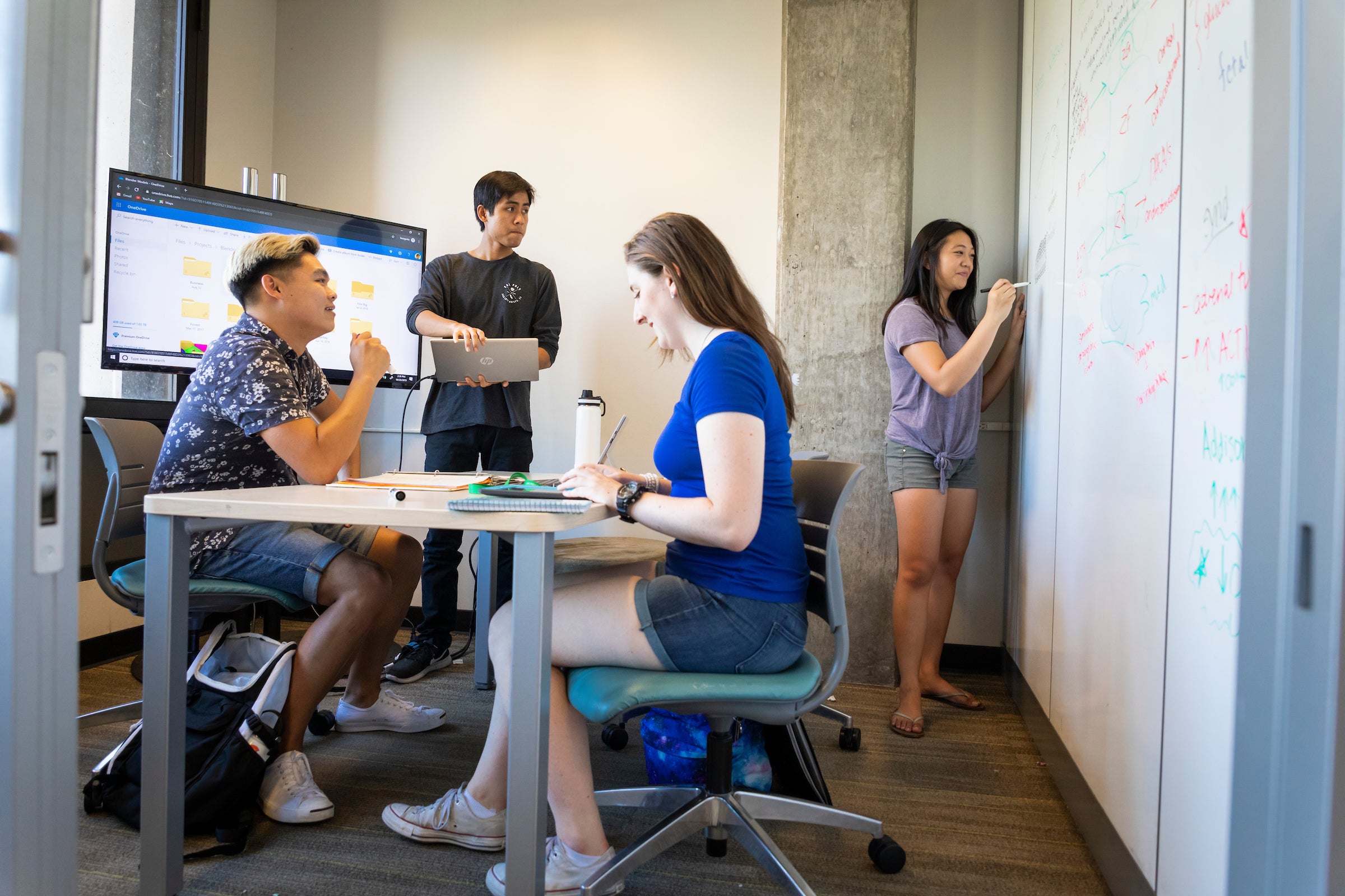 A group of four students spaced apart and working in a Kennedy Library fishbowl