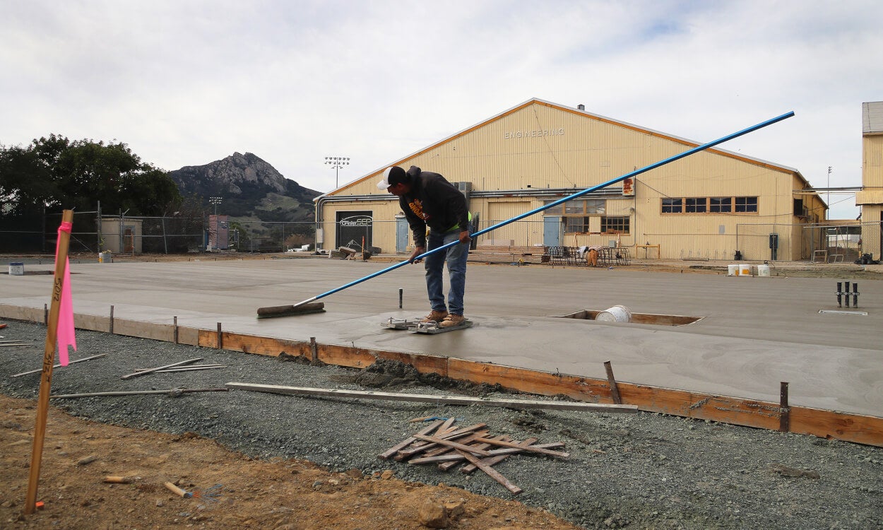 A construction worker oversees the process of concrete being poured to create an outdoor workspace at the Hangar