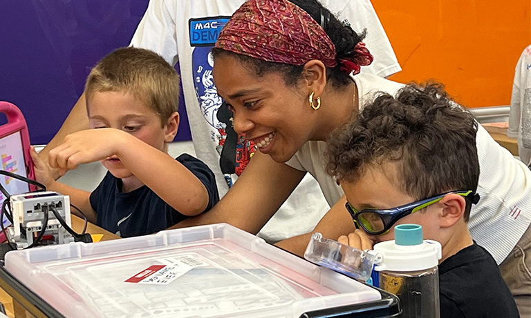 A woman helping two elementary school students with their projects