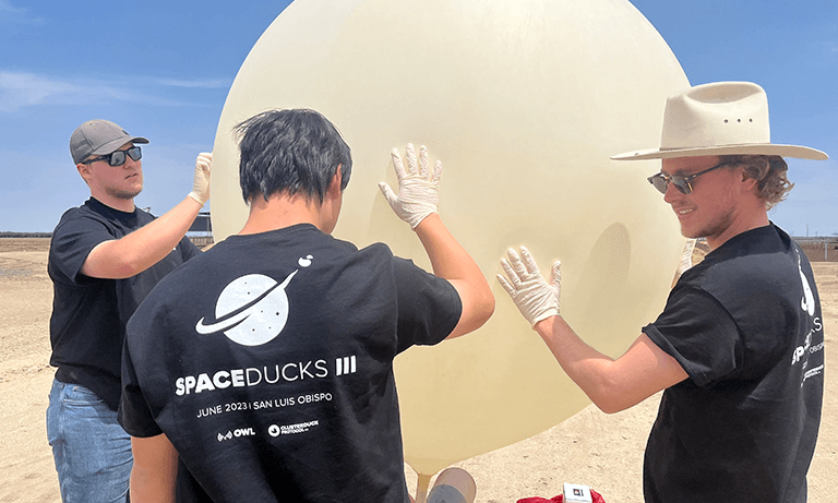 Three people grabbing onto a giant balloon before launching it into the air