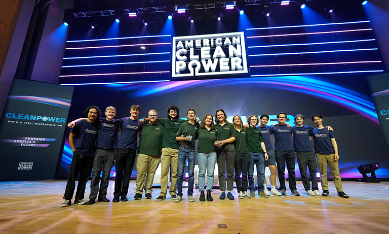 Students on a big stage smiling and holding a trophy