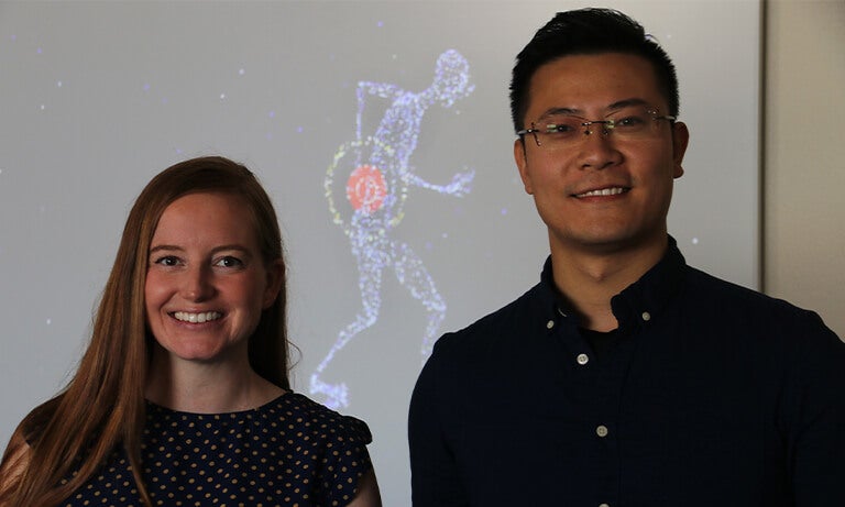 Two professors stand in front of back pain graphic
