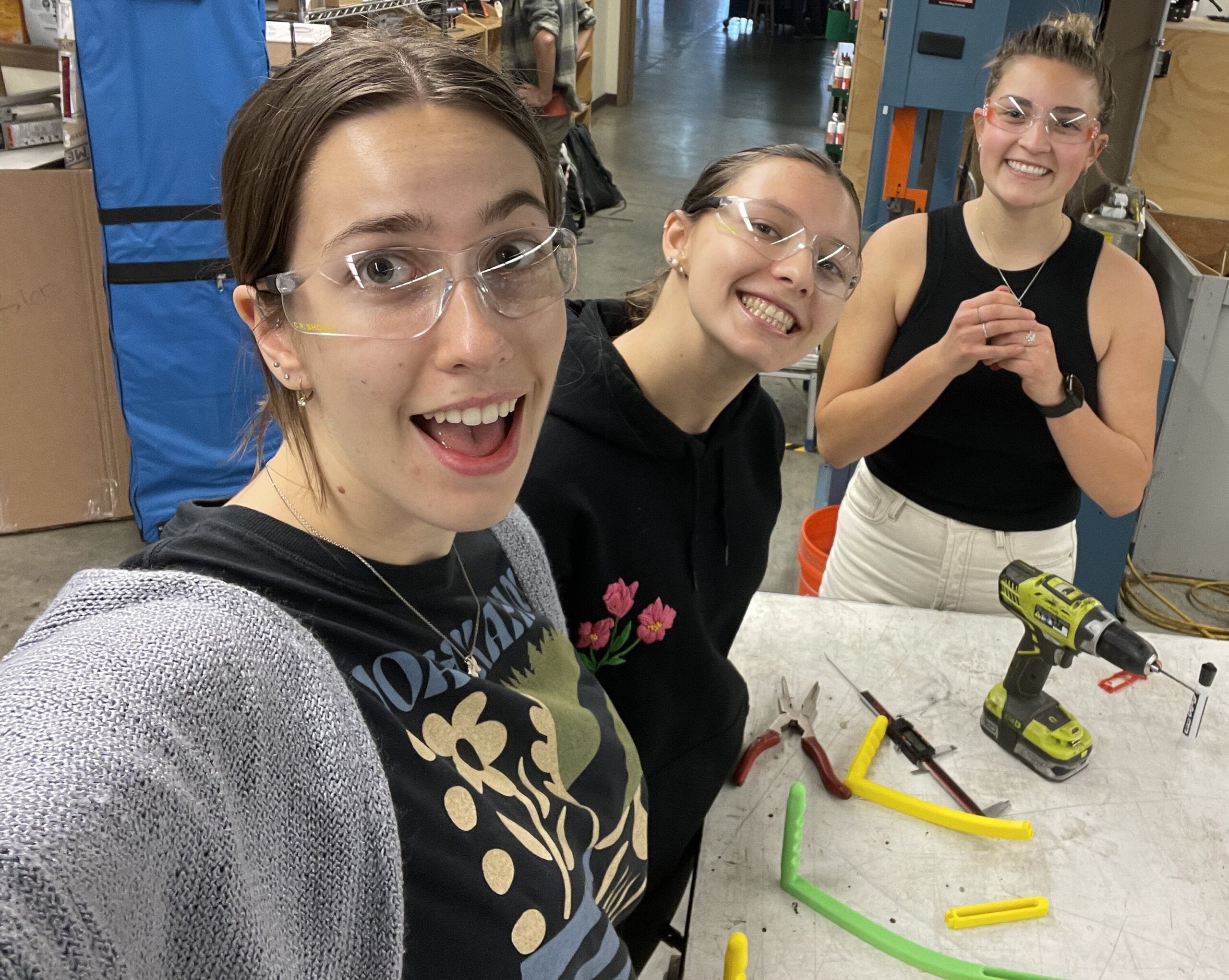 Three students take a selfie in the Mustang '60 machine shop as they manufacture their assisted birth device