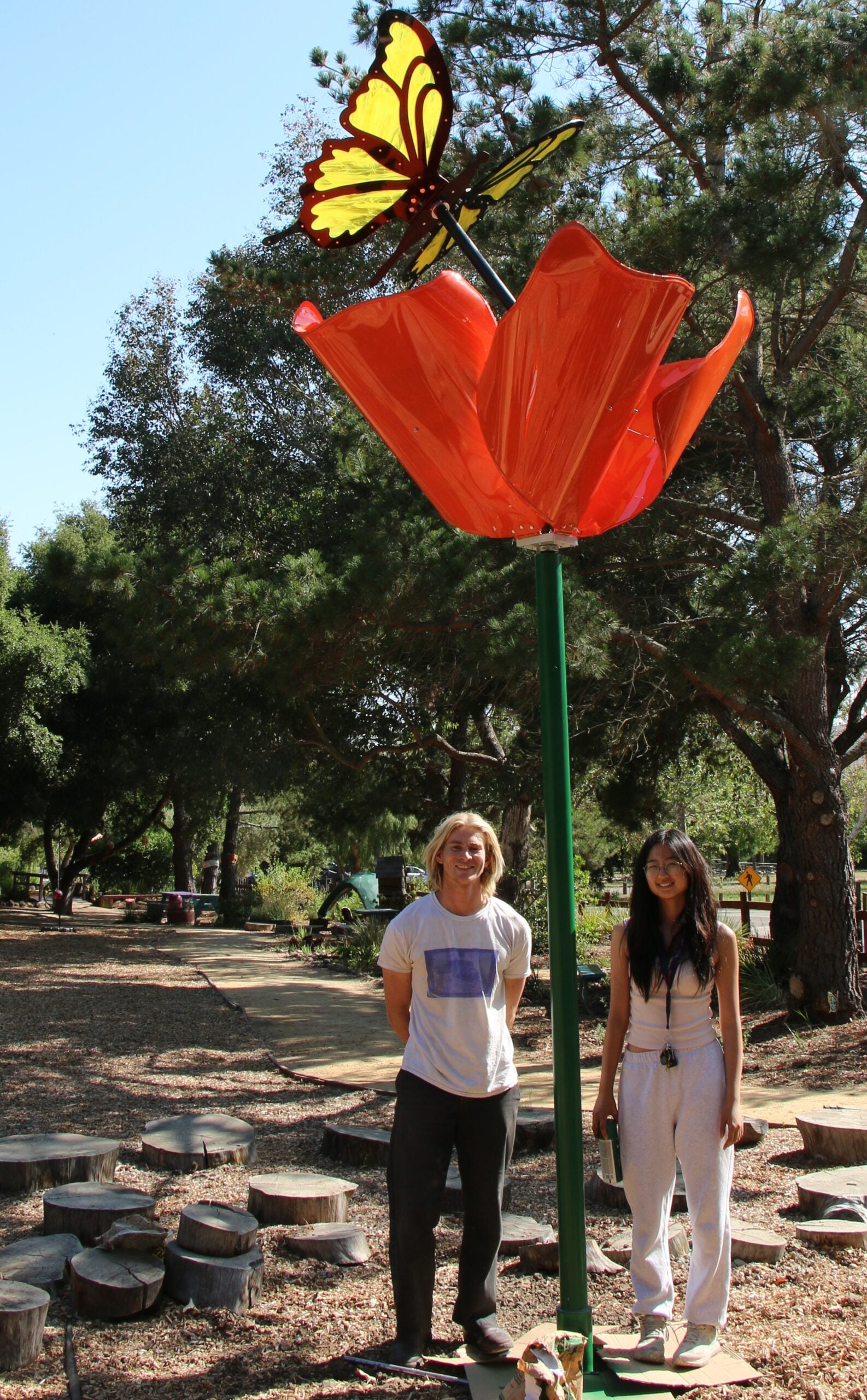 Students stand beneath their poppy and butterfly sculpture