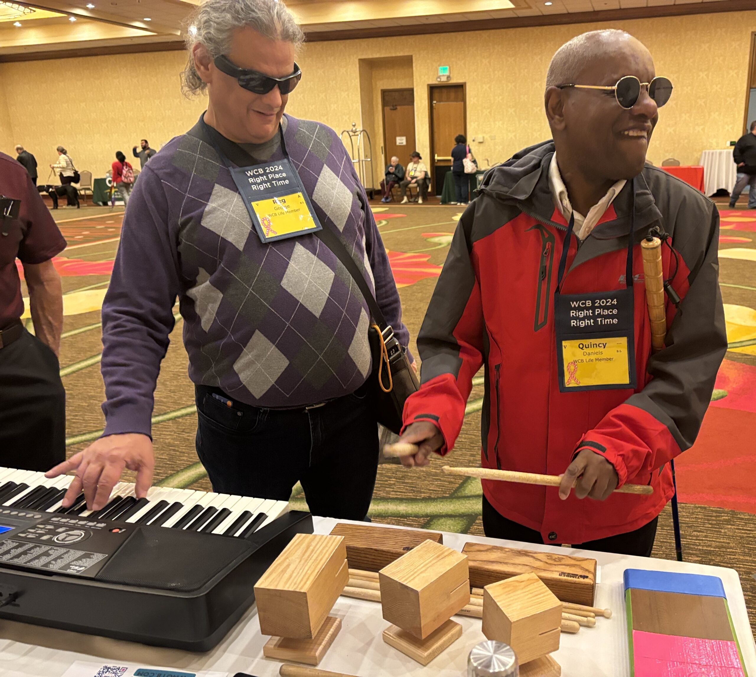 One musician plays a keyboard while the other taps a wooden block