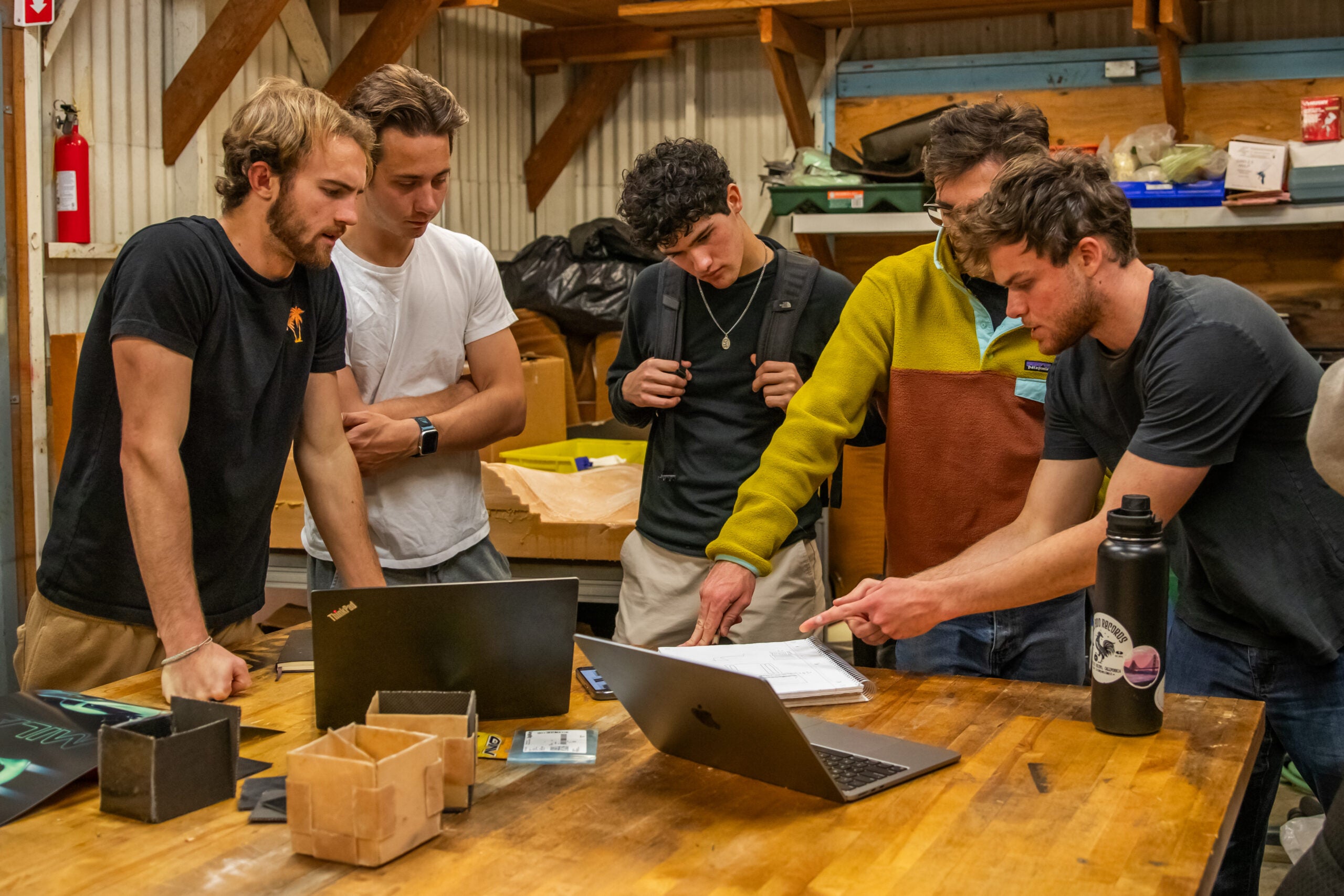 Members gather around notebooks and laptops as they work on the design of their electric car