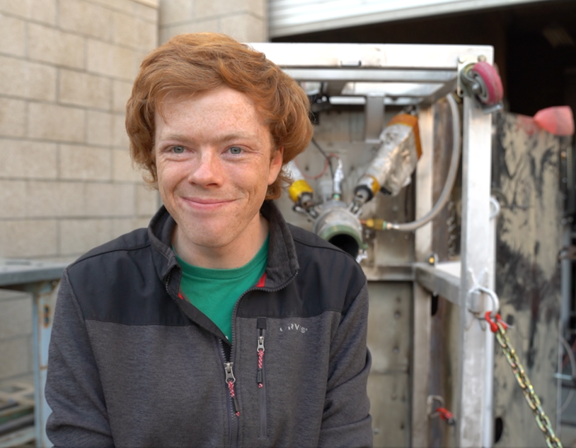 Student stands in front of the test stand and rocket engine setup