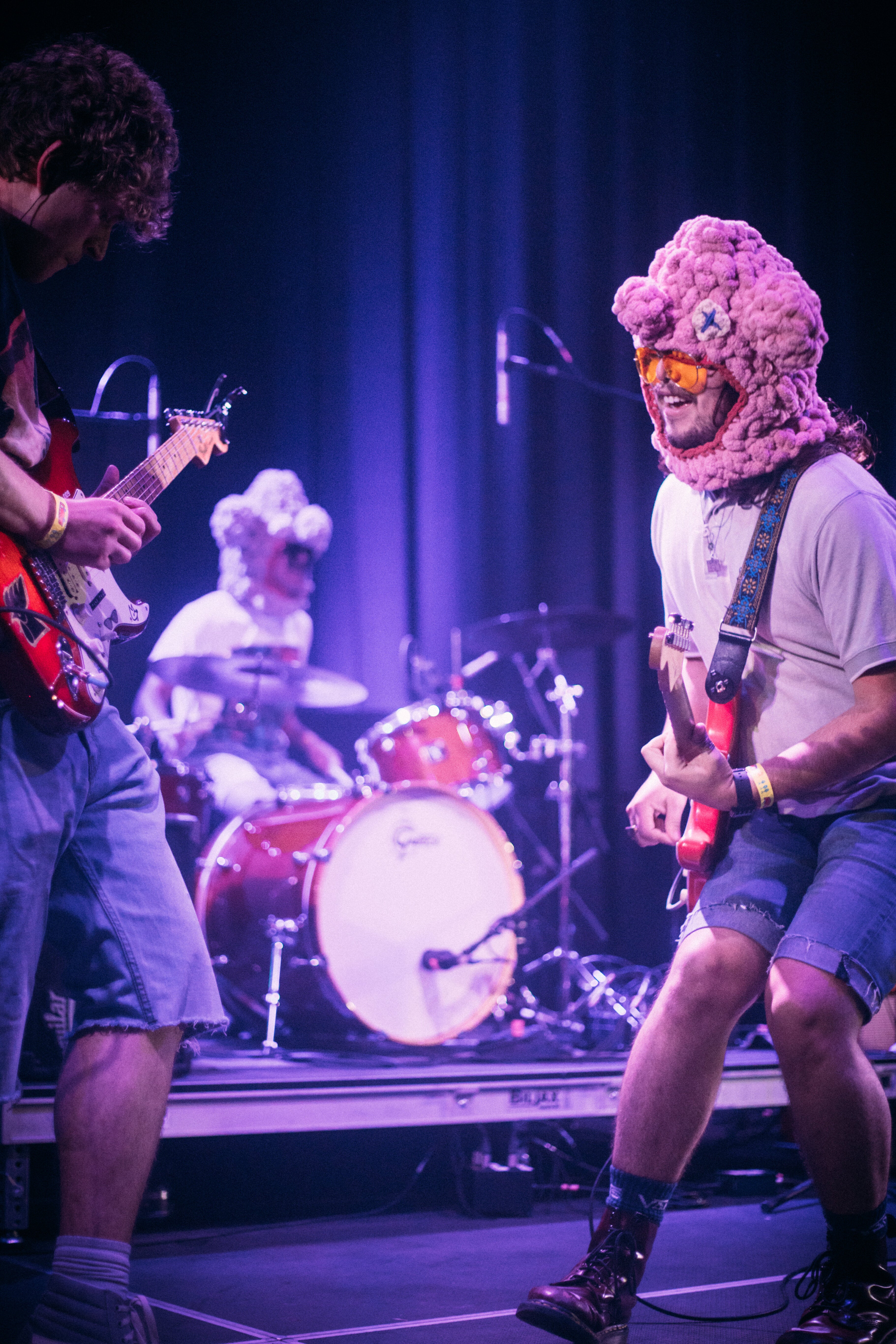 Two band members play guitar while a third plays drums on stage