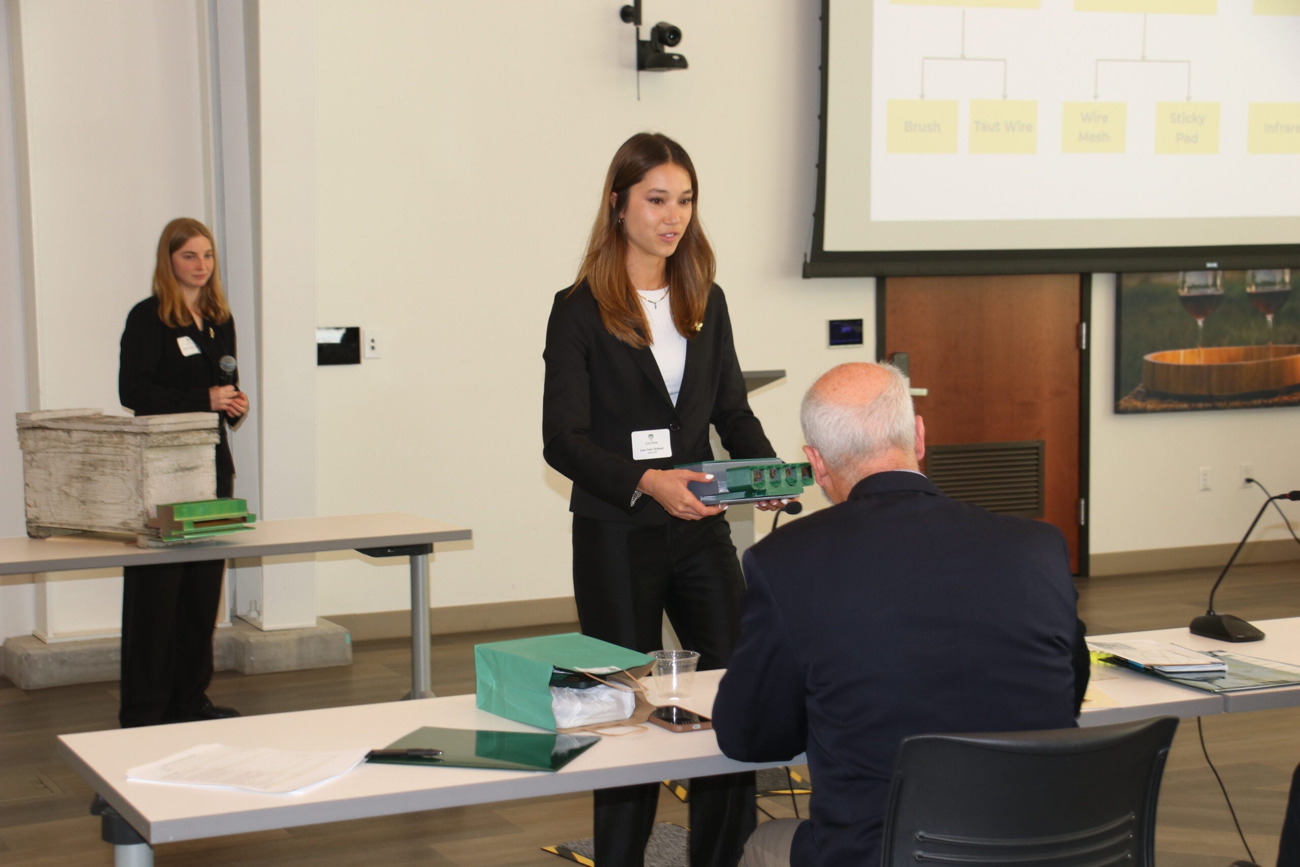 A student handing over a product prototype to a competition judge.