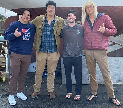 Four students stand next to sailboat