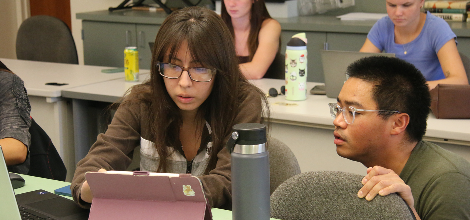 Lecturer works with student on laptop in classroom
