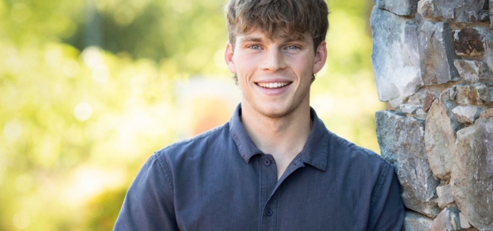 Headshot of a Cal Poly student leaning against a tree with foliage in the background