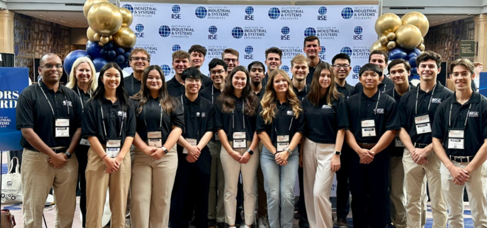 Students and faculty members posing for a group photo in front of a step and repeat banner at a conference.