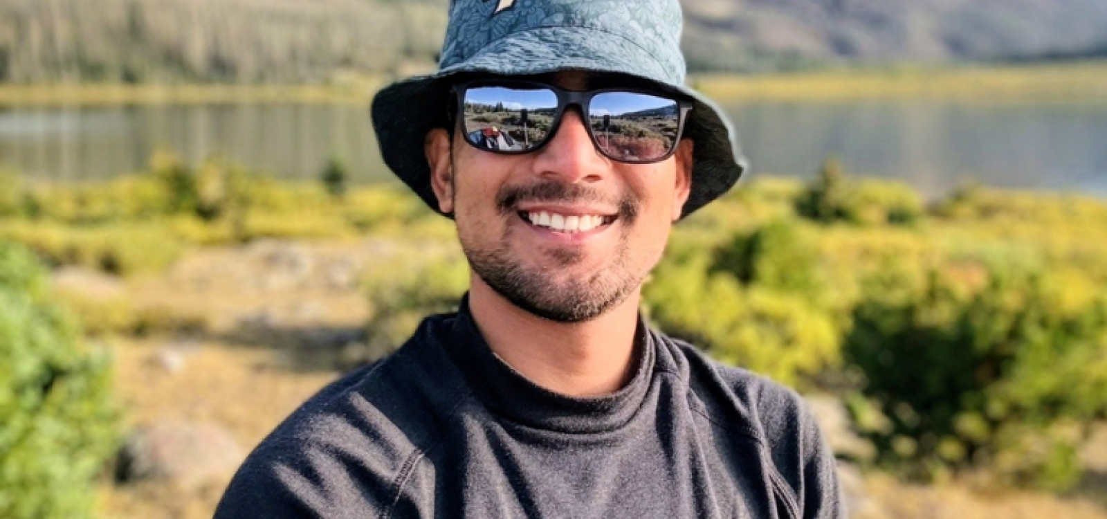 A man wearing a hat and sunglasses smiling at the camera
