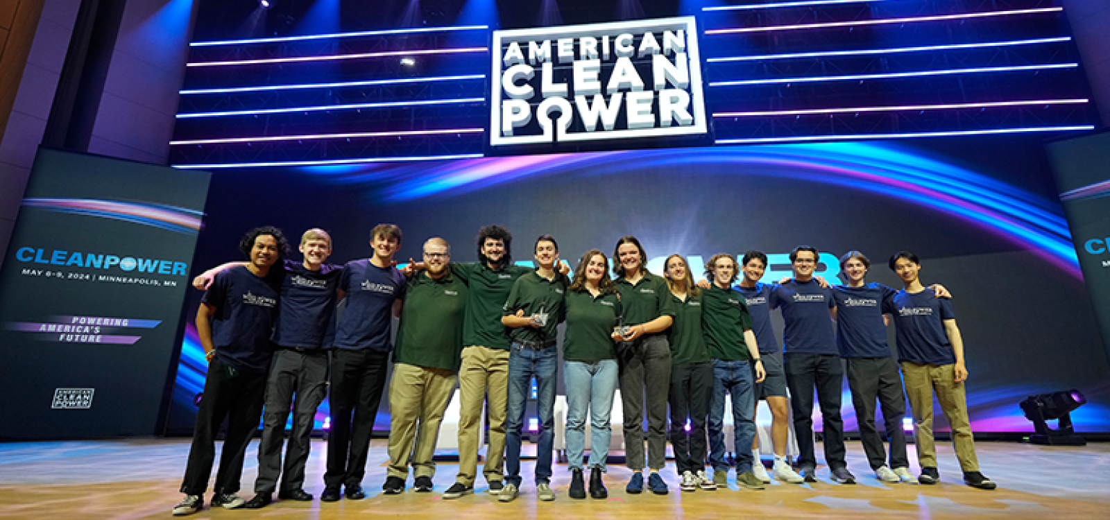 Students on a big stage smiling and holding a trophy