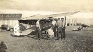 Cal Poly students confer beside a biplane at Clark Field in San Luis Obispo, reflecting the program’s early ties to flight.