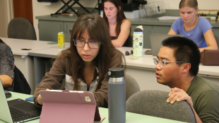 Lecturer works with student on laptop in classroom