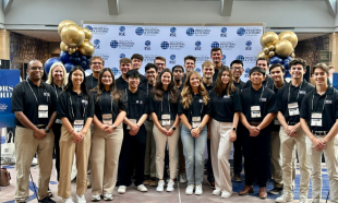 Students and faculty members posing for a group photo in front of a step and repeat banner at a conference.