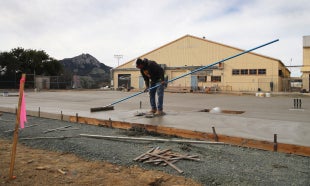 A construction worker oversees the process of concrete being poured to create an outdoor workspace at the Hangar