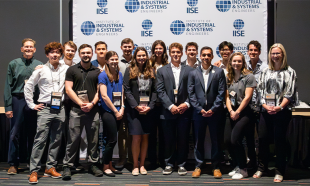 A group of people standing in front of a large event banner smiling