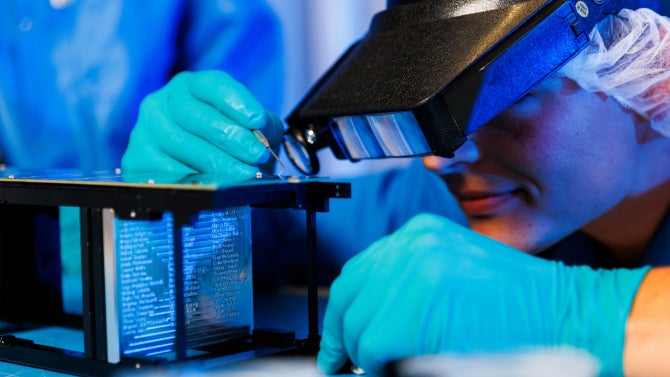 student assembles the structure of the CubeSat satellite in a cleanroom on campus