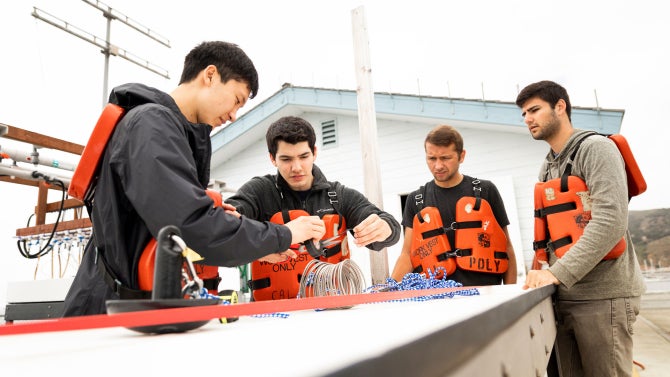 materials engineering students work with two titanium coils which they are testing out at the Cal Poly Pier to see how suitable the material is for use as an artificial reef.
