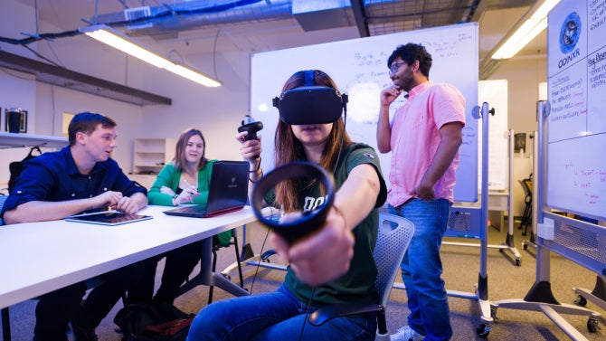 student wearing vr glasses and handset with student talking in background