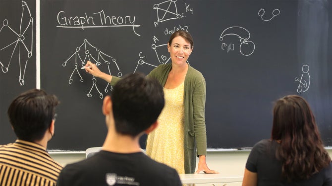 professor teaches graph theory at chalkboard with students in the foreground