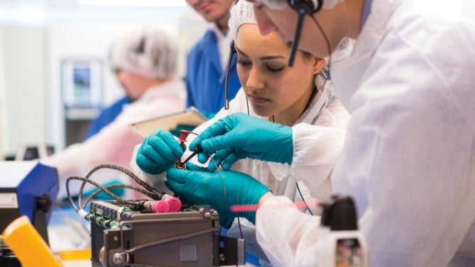 students in protective gear work carefully on cubesat with lab instruments