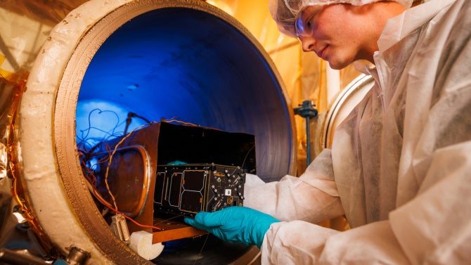 CubeSat team member in the thermal vacuum chamber room with a CubeSat