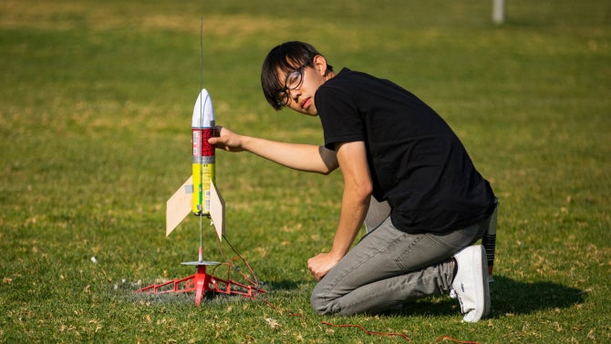aerospace student holding model rocket in grass field during competition.