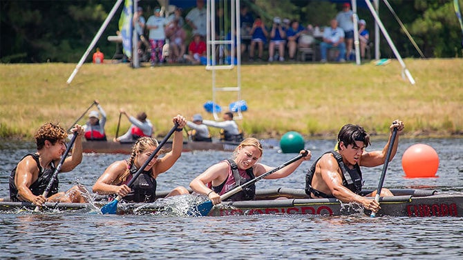 four students paddle furiously in concrete canoe during competition