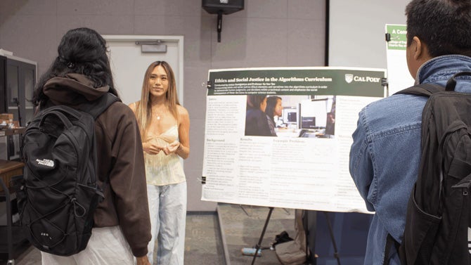 two students talking to student in front of her poster