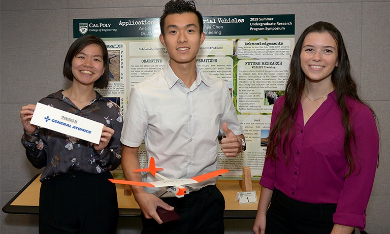 Three students in front of poster
