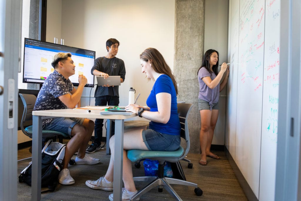 A group of four students spaced apart and working in a Kennedy Library fishbowl