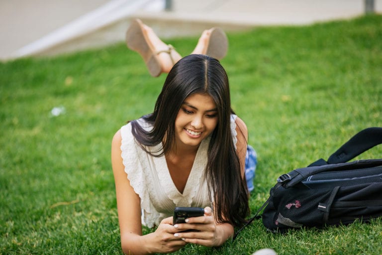 Student outdoors on a grassy lawn with mobile device