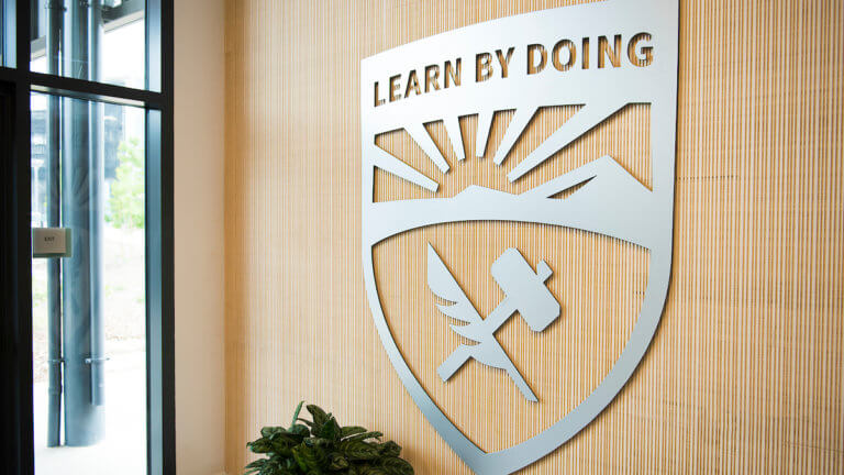 Perspective view of metalic Cal Poly shield mounted on wood grain wall
