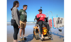Surfer in wheelchair with man and woman standing nearby