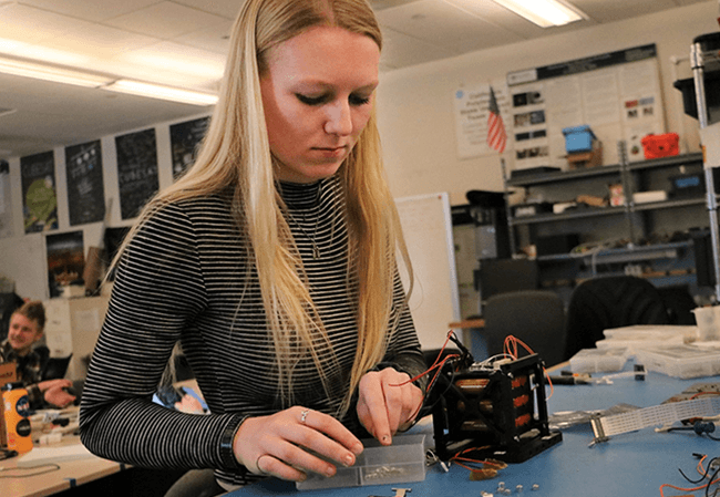 Aerospace engineering student Brigitte Petersen working on a CubeSat project on a workbench inside the PolySat lab
