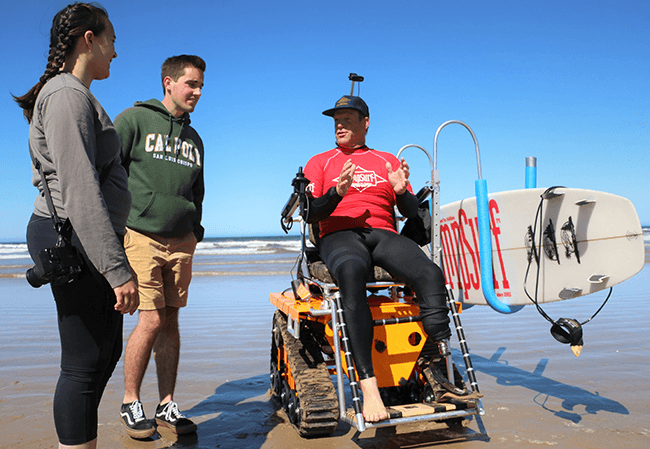 Materials Engineering student Caitlin Tang-Hornbuckle and Electrical Engineering student Josh Simpson discuss the adaptive wheelchair project with AmpSurf founder and president Dana Cummings on a sunny day at the beach