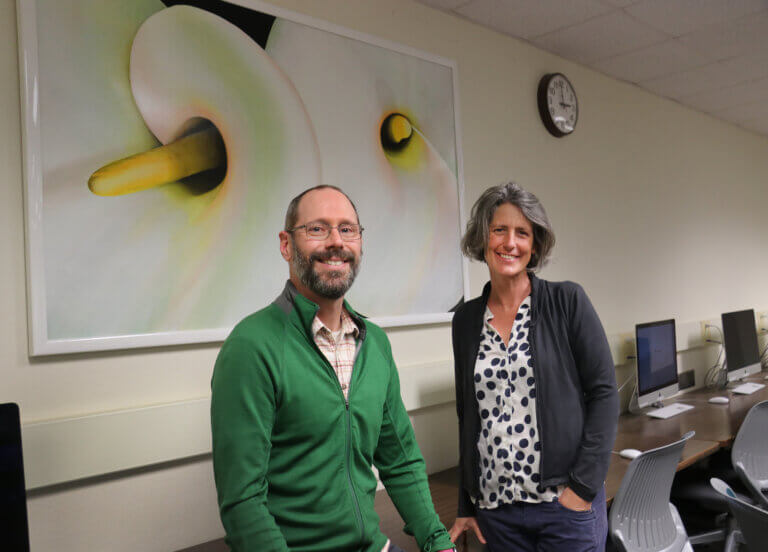 Annie Armstrong's calla lilies painting now adorns the main computing lab, pictured here with department chair Chris Lupo and professor Zoë Wood