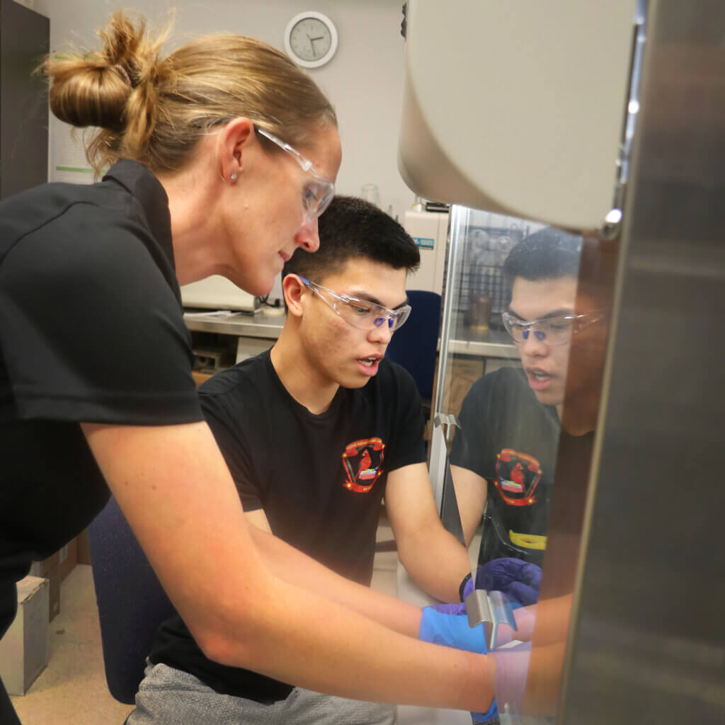 Professor Kristen Cardinal, left, and biomedical engineering student Squeaky Buentipo operate a new Spinbox machine that produces electro-spun sheets that serve as scaffolding for growing blood vessels.