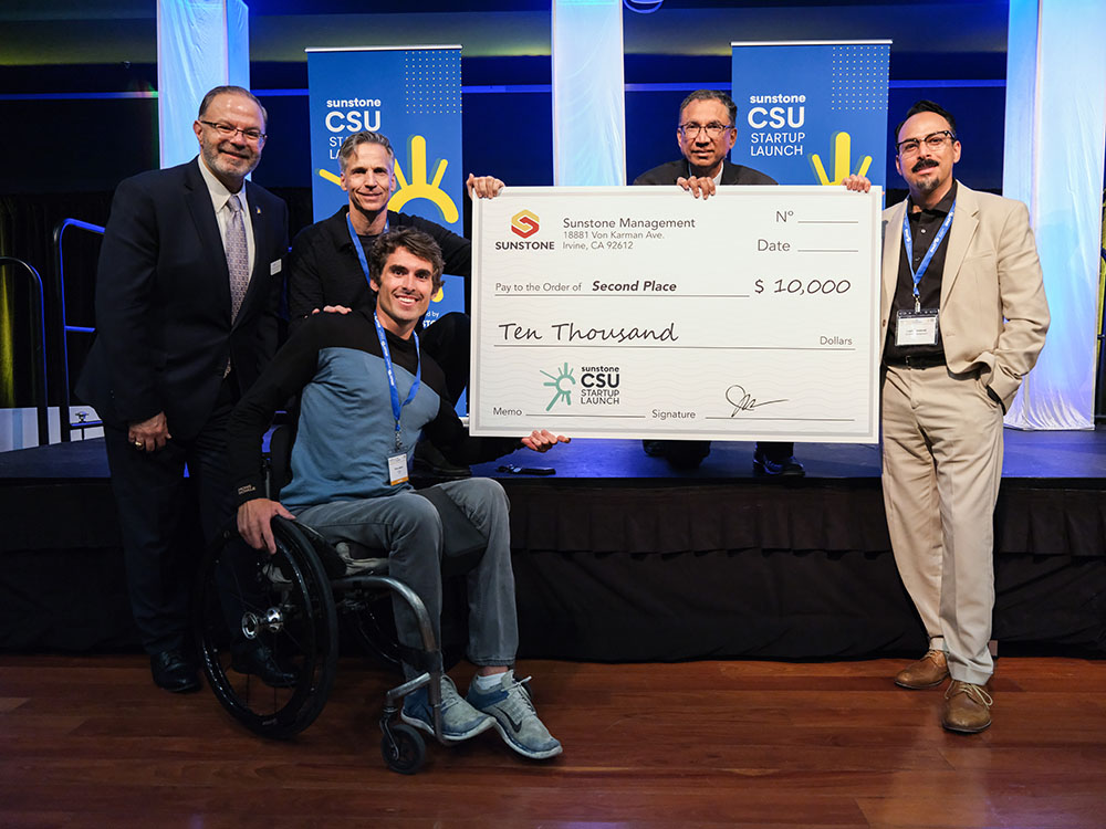 Recent graduate holds a check for $10,000 after winning a startup competition